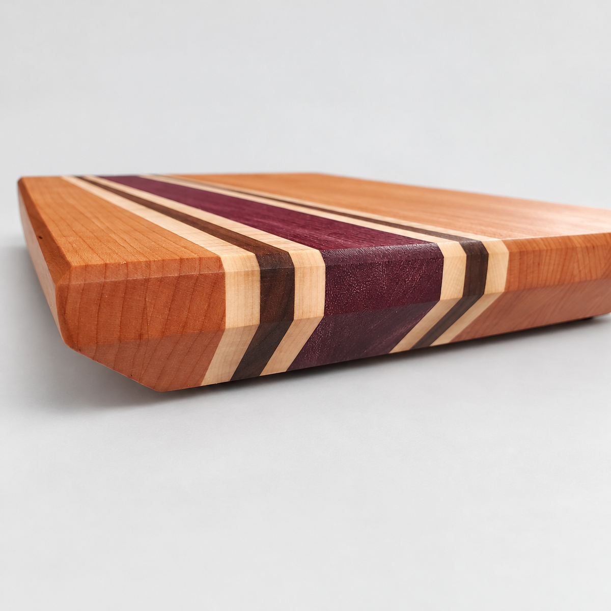 Handcrafted Cherry, Purple Heart, Walnut & Curly Maple Cutting Board, detail view on a light gray background